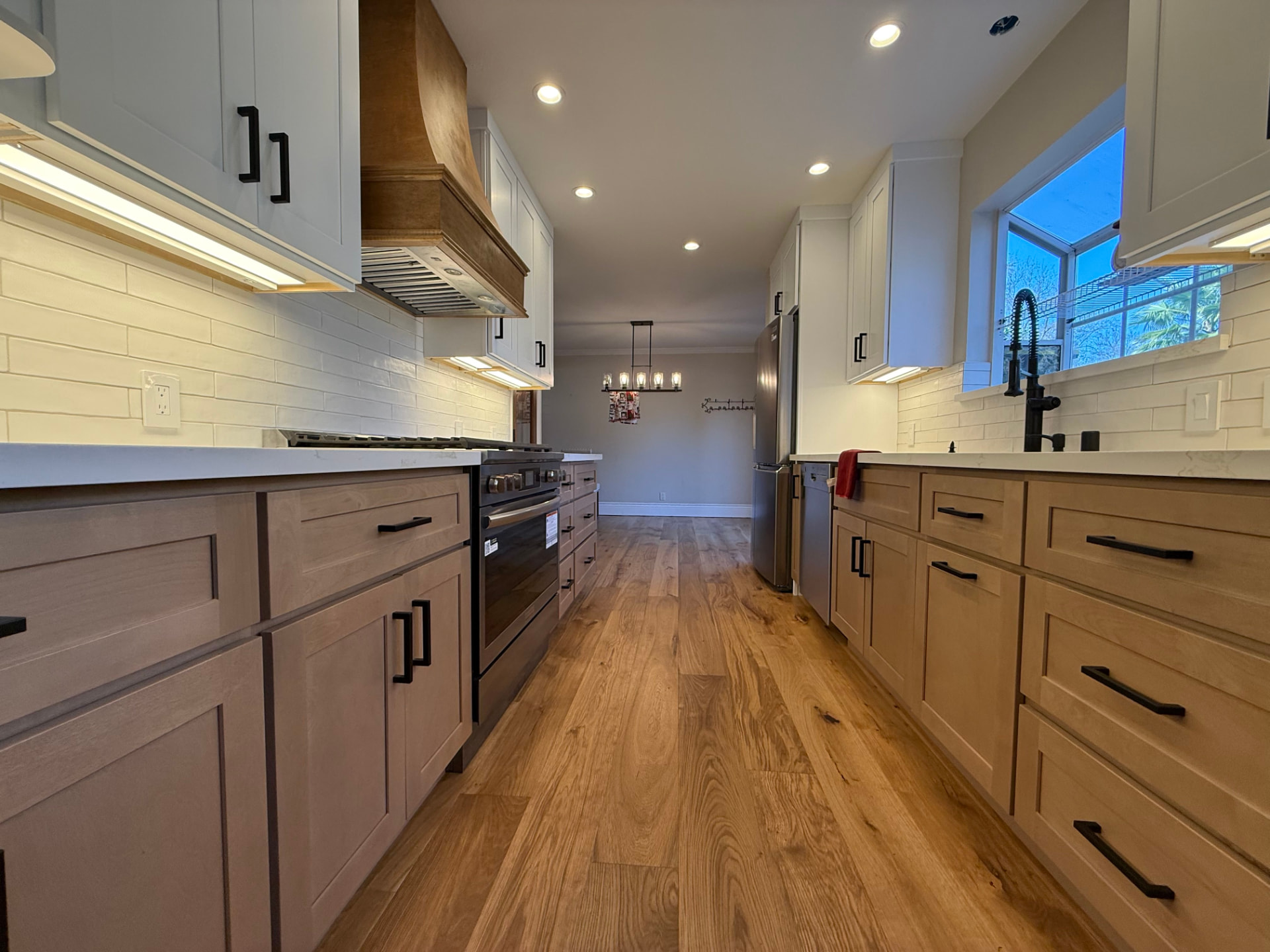 Kitchen remodel by The House Doctor with natural wood floors, white cabinets, and a range hood